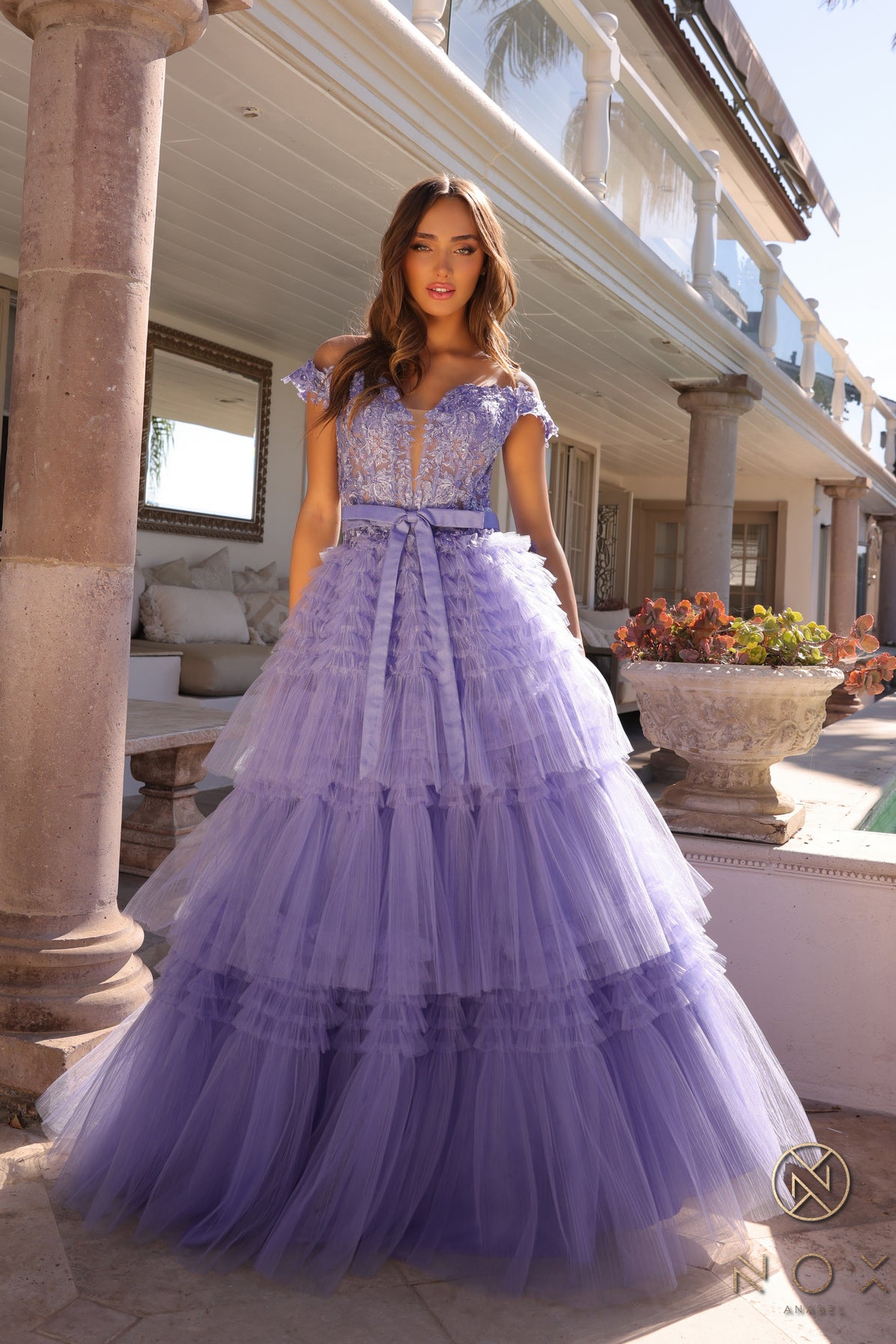 Experience the elegance and sophistication of the Nox Anabel E1293 Prom Dress. With a stunning A-line silhouette, pleated tulle layers, and sheer lace embellished Corset , this dress will make heads turn. Complete with an off-shoulder design and a delicate bow, this dress is perfect for a prom or any formal event.  Sizes: 0-16  Colors: Blue, Mauve, Mint Green, Periwinkle