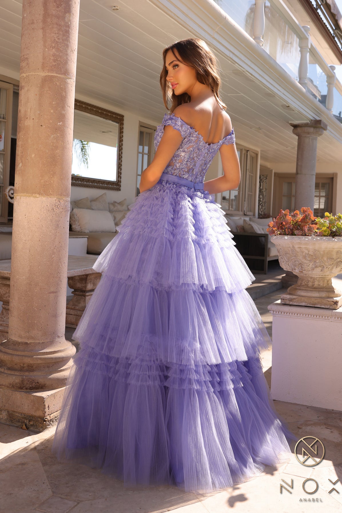 Experience the elegance and sophistication of the Nox Anabel E1293 Prom Dress. With a stunning A-line silhouette, pleated tulle layers, and sheer lace embellished Corset , this dress will make heads turn. Complete with an off-shoulder design and a delicate bow, this dress is perfect for a prom or any formal event.  Sizes: 0-16  Colors: Blue, Mauve, Mint Green, Periwinkle