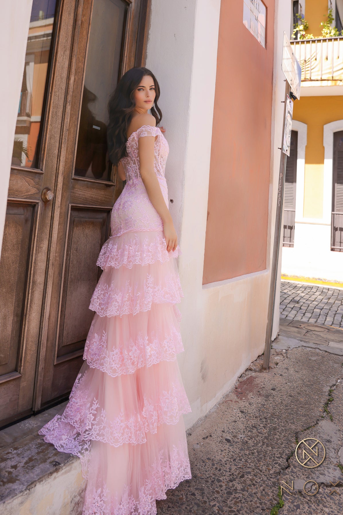 Nox Anabel R1301 is a Lonf Fit & Flare Asymmetrical Ruffle Sequin high slit Slit Prom Dress. Featuring a Sheer Lace off the shoulder Corset. Layered tulle skirt with train and lace edges.  Sizes: 0-16  Colors: Blush, Black, Red, Victorian Lilac 