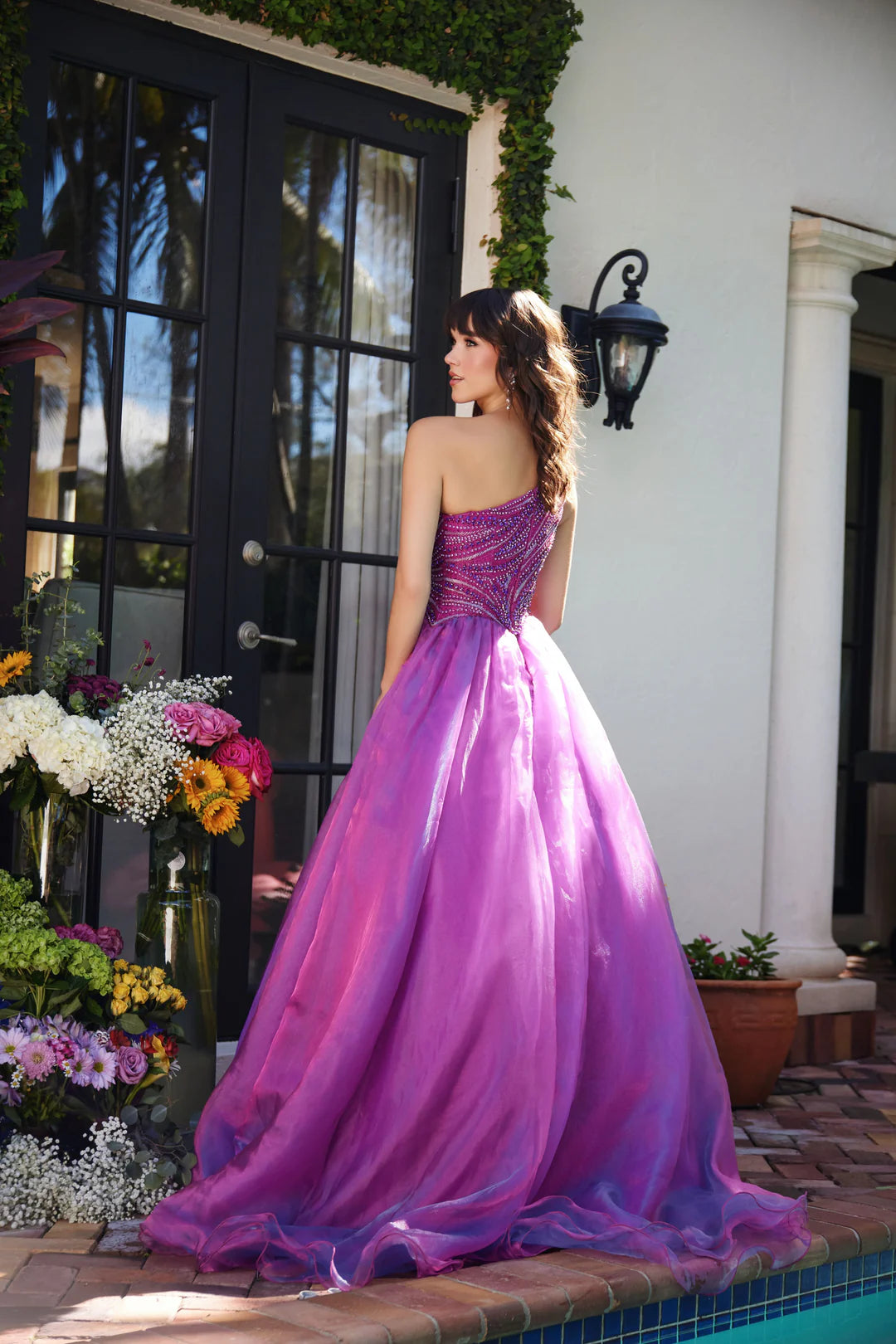 This Ava Presley gown, style 29258, exudes a captivating elegance with its magenta hue and one-shoulder design. The asymmetrical neckline adds a modern touch, while the fitted bodice features intricate beadwork in swirling patterns that accentuate the curves and create a sparkling effect.&nbsp;The full skirt is crafted from layers of lightweight fabric that flow gracefully, adding movement and volume to the gown. This design is perfect for formal events like proms, pageants, or gala evenings, offering a ble