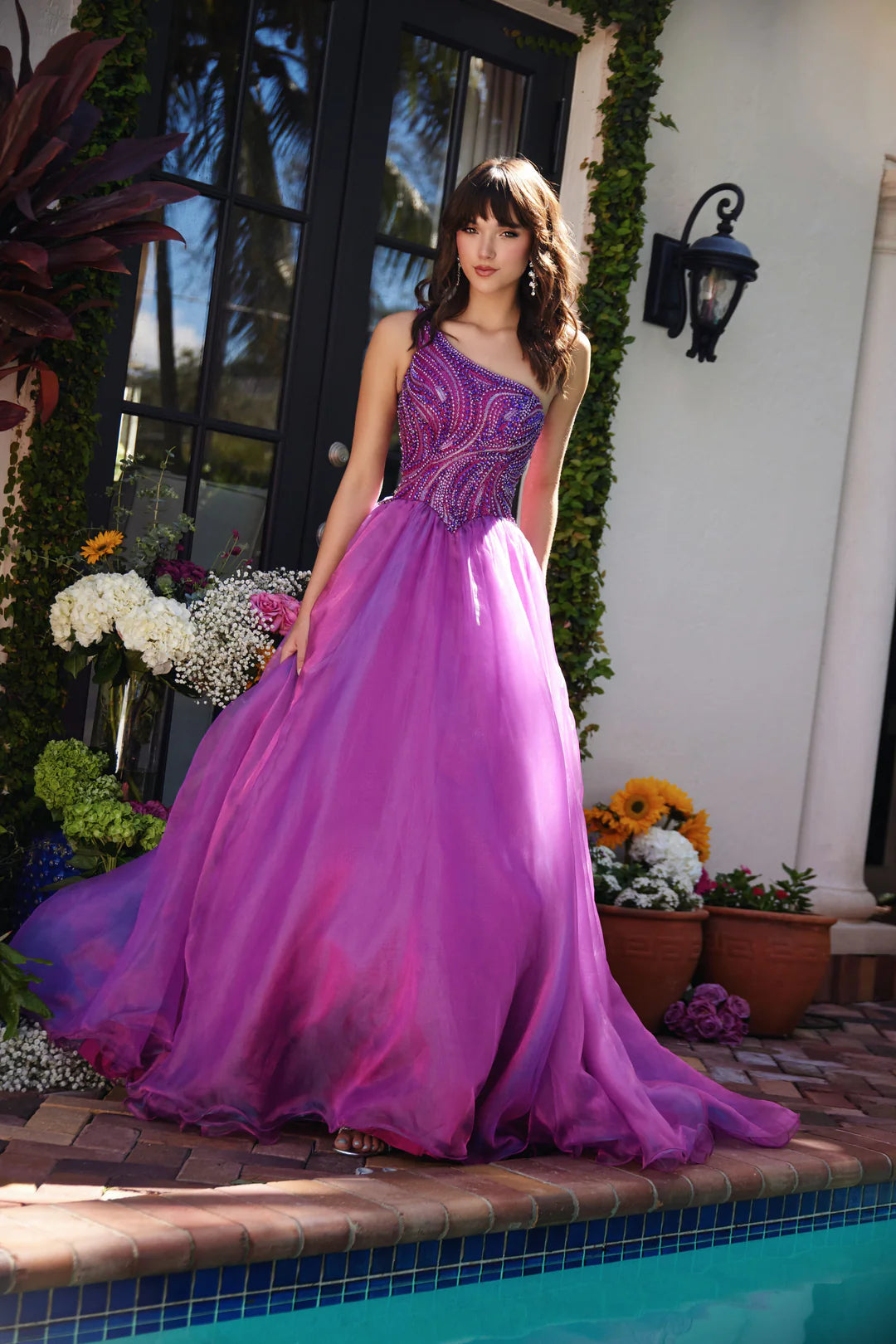 This Ava Presley gown, style 29258, exudes a captivating elegance with its magenta hue and one-shoulder design. The asymmetrical neckline adds a modern touch, while the fitted bodice features intricate beadwork in swirling patterns that accentuate the curves and create a sparkling effect.&nbsp;The full skirt is crafted from layers of lightweight fabric that flow gracefully, adding movement and volume to the gown. This design is perfect for formal events like proms, pageants, or gala evenings, offering a ble