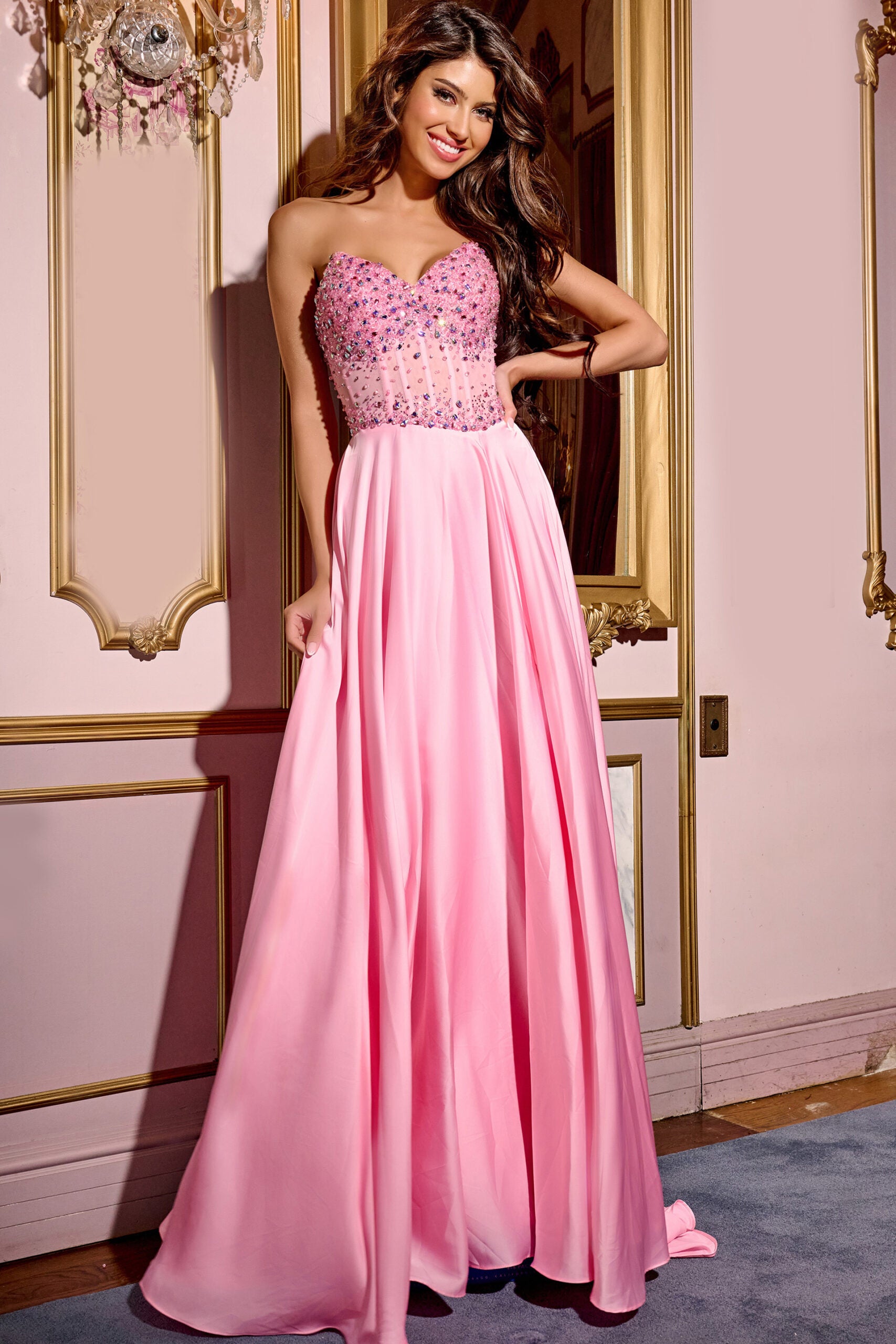 This Jovani D6021 floor-length gown features a structured sweetheart neckline, offering a flattering silhouette with its sleeveless design. The bodice is intricately embellished with scattered rhinestone accents that provide a delicate yet detailed appearance. The back of the dress is fitted and closed. The A-line skirt flows seamlessly from the fitted bodice into a voluminous chiffon train, creating graceful movement. The full-length chiffon skirt has a soft, flowing drape that enhances the dress’s airy ae