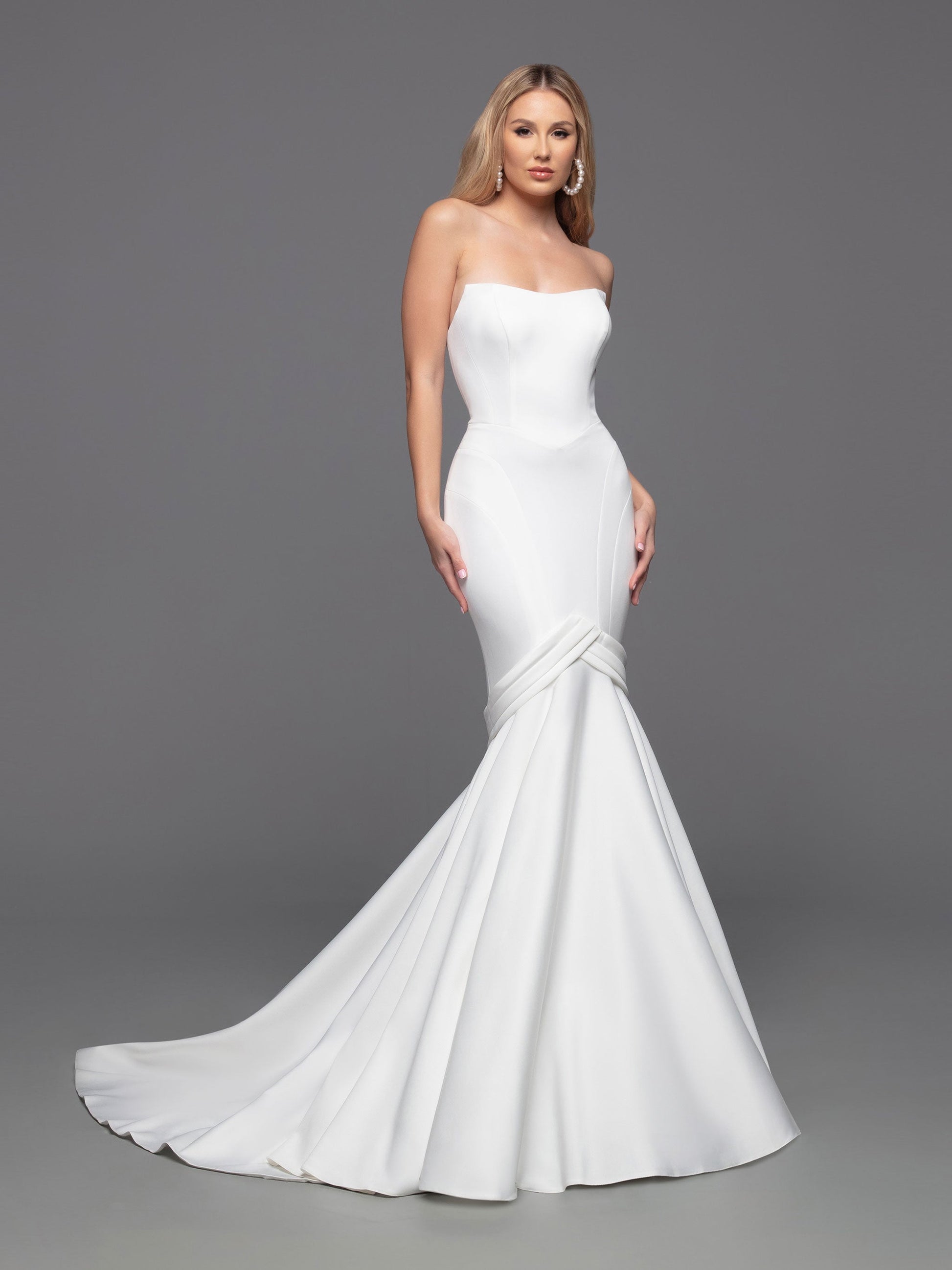 Experience an unforgettable wedding day with this luxurious bridal gown from Davinci. Crafted from alluring ivory fabric, this fit-and-flare mermaid gown is perfected with a strapless, straight-across neckline, a modest silhouette, and an open back with interesting button details and a zipper fastening. The chapel train adds a truly elegant touch.