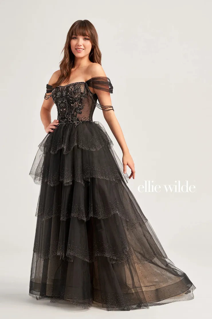 The Ellie Wilde EW35040 prom dress boasts a stunning A-line silhouette adorned with sparkling crystals and sequins. The sheer corset bodice adds a touch of allure, while the off-the-shoulder neckline and beaded fringe details add a trendy touch. Elevate your prom look with this enchanting and figure-flattering dress.  Sizes: 00-16  Colors: Slate, Black/Champagne