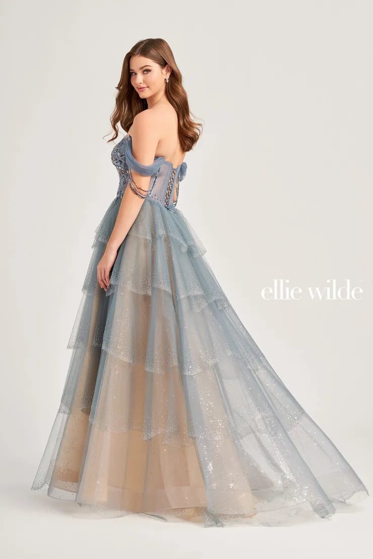 The Ellie Wilde EW35040 prom dress boasts a stunning A-line silhouette adorned with sparkling crystals and sequins. The sheer corset bodice adds a touch of allure, while the off-the-shoulder neckline and beaded fringe details add a trendy touch. Elevate your prom look with this enchanting and figure-flattering dress.  Sizes: 00-16  Colors: Slate, Black/Champagne