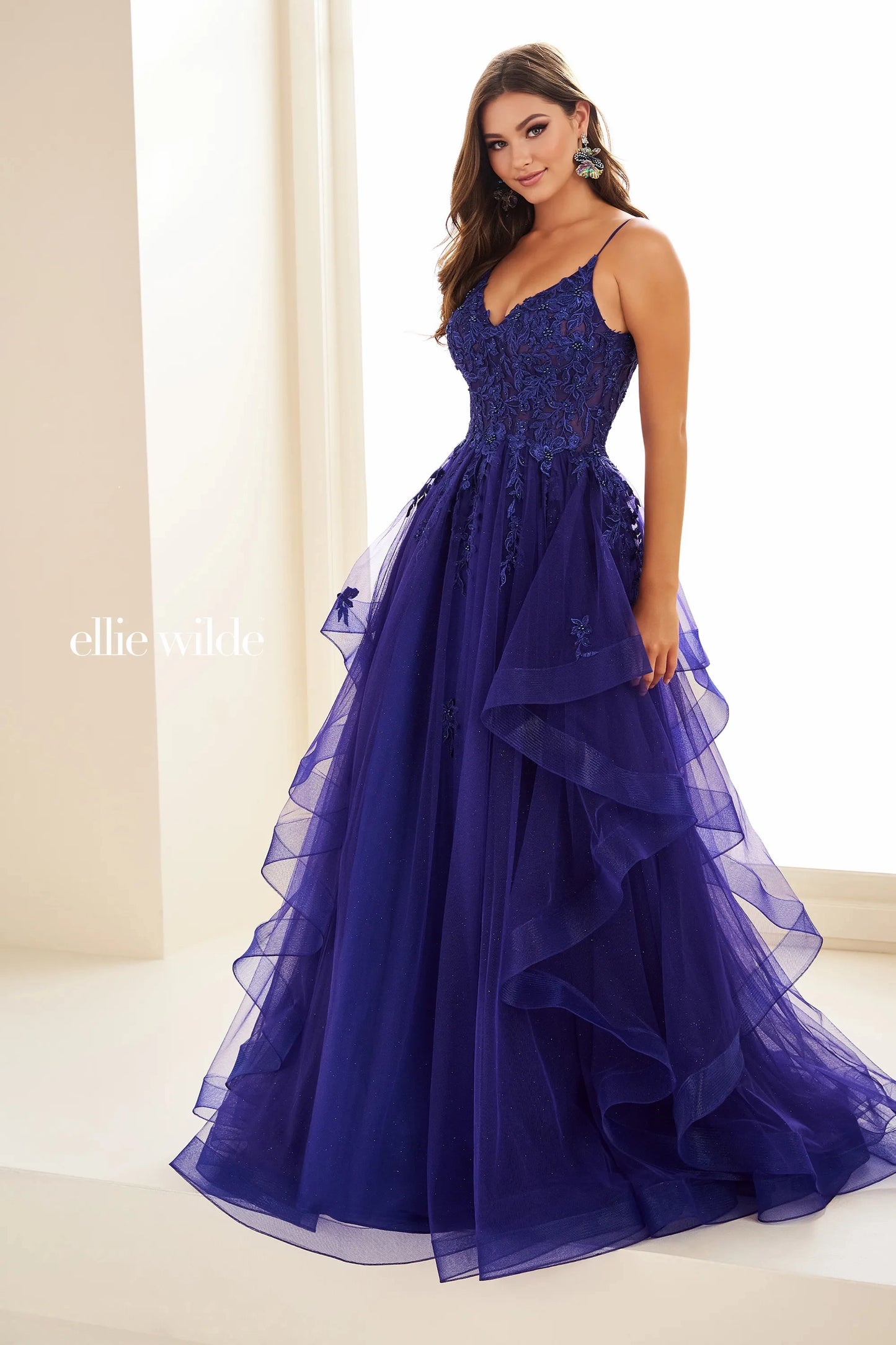 This Ellie Wilde EW3685 dress features sheer lace and a shimmering design for a glamorous look. The A-line silhouette flatters all body types, while the ruffle detailing adds a touch of elegance. Perfect for prom, formal events, and pageants.