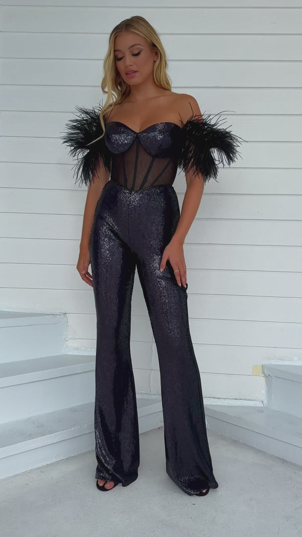 The Ava Presley 39577 Long Sequin Jumpsuit is designed to make you stand out at any formal event. The intricate sequin detailing and sheer corset add an alluring touch, while the feather off-the-shoulder sleeves add a touch of elegance. Perfect for pageants or other formal occasions.  Sizes: 00-16  Colors: Black/AB, Iridescent White, Light Blue