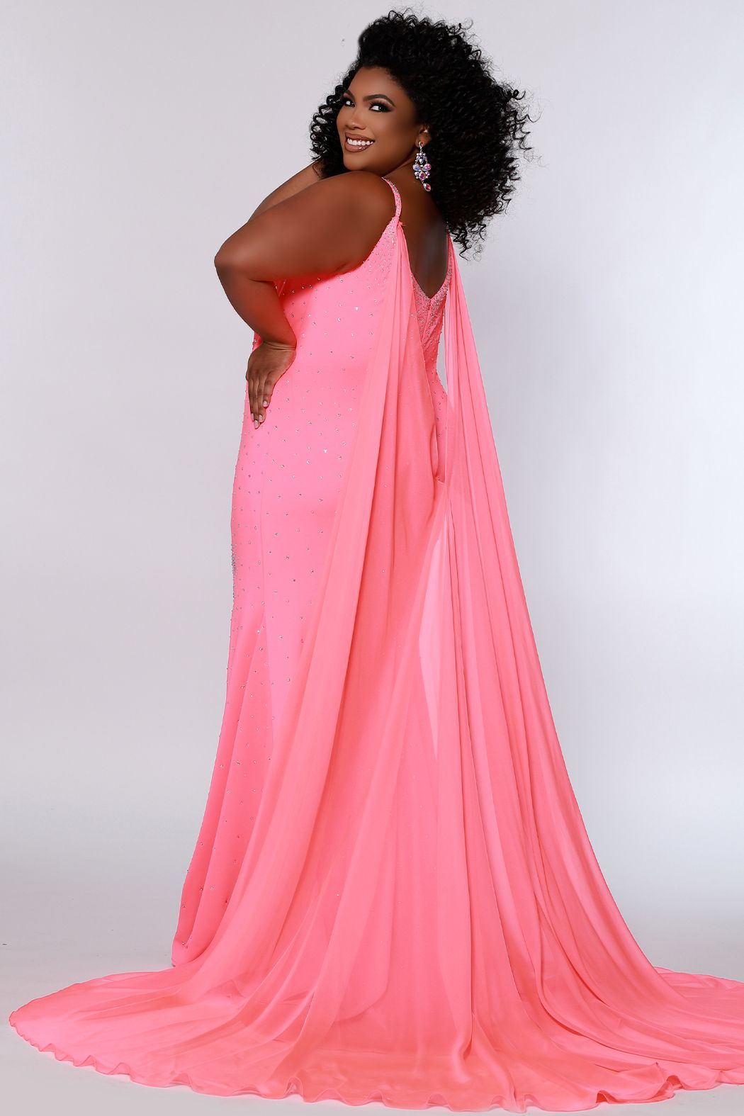 Johnathan Kayne for Sydney's Closet JK2218 Maverick Plus Sized Prom, Pageant and Formal Evening Wear Dress with Cape Buckle up because this gown is a hot one! The stretch heavy knit in this slim fit princess line silhouette and deep v-neckline makes showing off your curves a power move! Sexy from head to toe in Deep Red, Hot Coral, and White Ice, you'll catch the light with sparkling stones throughout the gown. Detachable chiffon scarves are the final winning moment and will fly as you strut!﻿