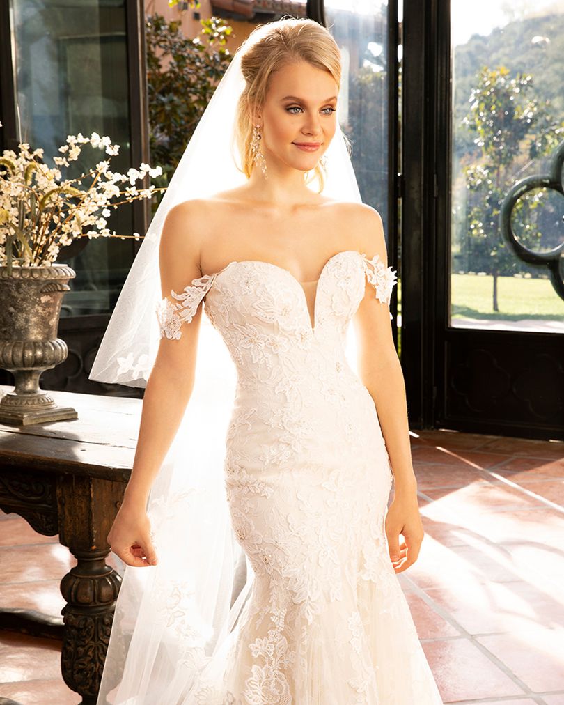 Style 2376 KARINA by Casablanca Bridal is a glamorous twist on the classic lace wedding dress. Off-shoulder sleeves transition into a classic sweetheart neckline, while floral lace swirls all throughout the fit-and-flare silhouette. The illusion back, lined with a row of subtle crystal buttons, transitions flawlessly into a gently scalloped train. A matching, two-tier cathedral length veil is available for the bride who wants to make an extra remarkable impact.  Size: 10, 14, 20  Ivory/Nude/Ivory/Silver